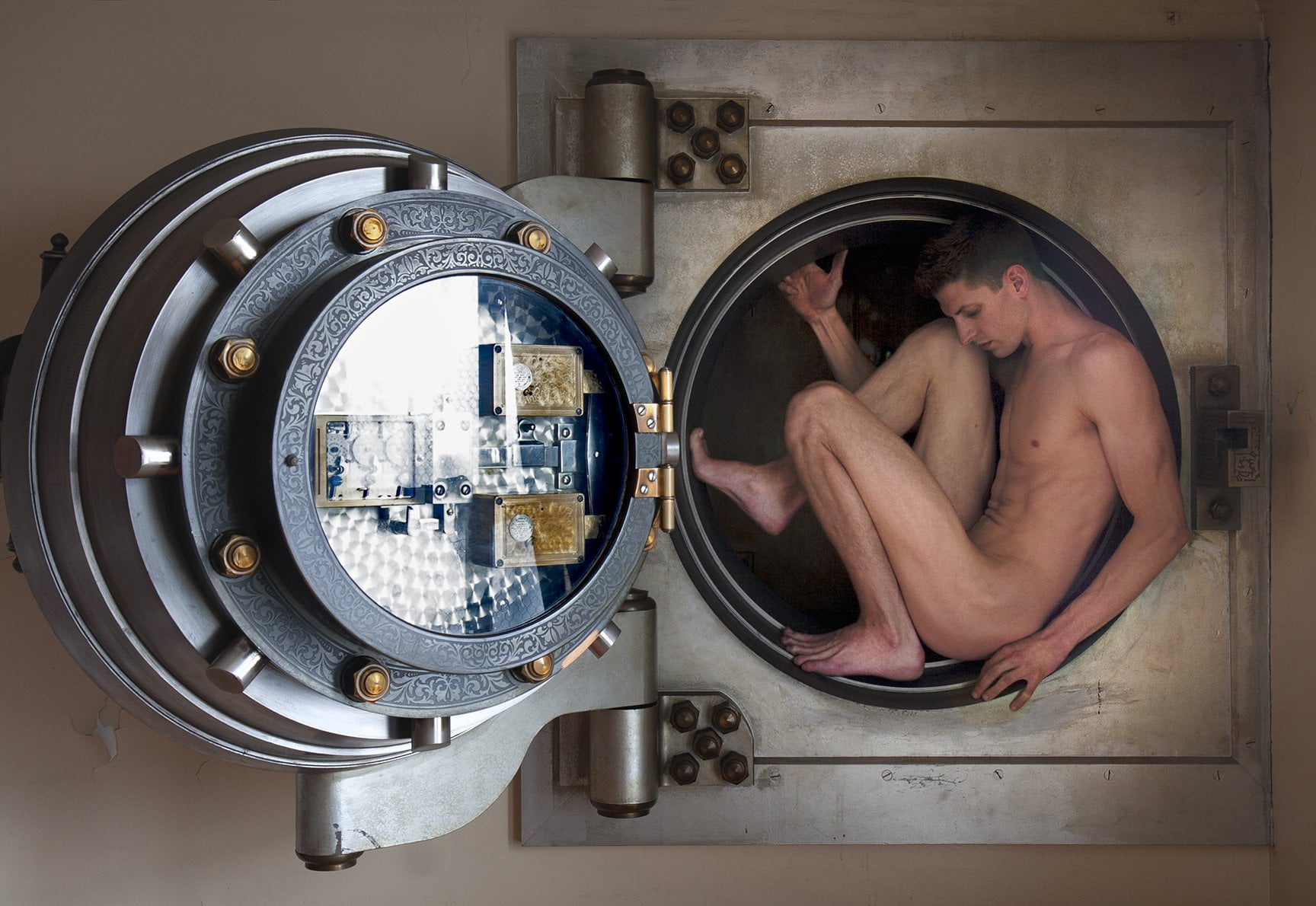 Nude male curled up in small bank vault opening
