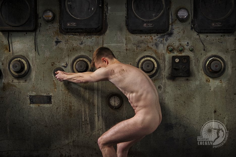 nude man pulling on lever in front of old control panel in abandoned factory