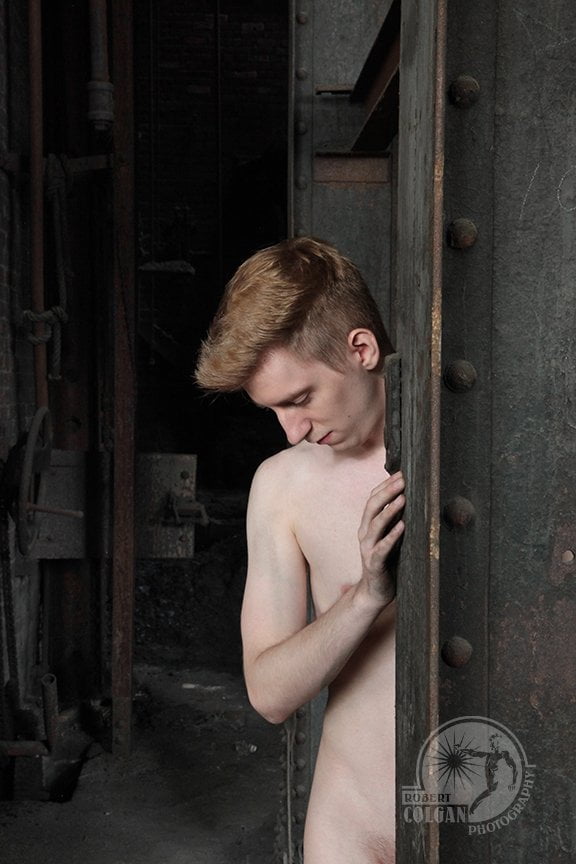 nude man standing, partially hidden behind I-beam