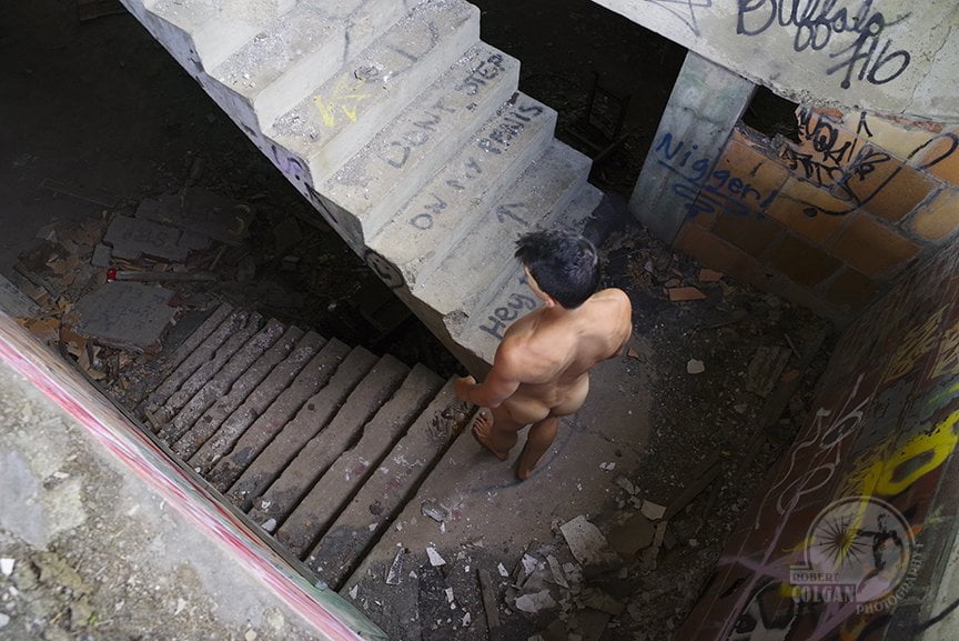 View looking down on nude man standing on landing between two sets of stairs