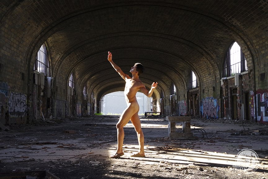 nude man raising hand to block the sunshine coming through the windows of an abandoned train station