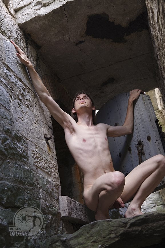 nude man crouching in front of old wooden door at old fort