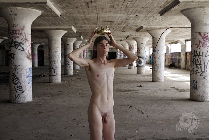 nude man standing in abandoned warehouse holding a golden crown above his head