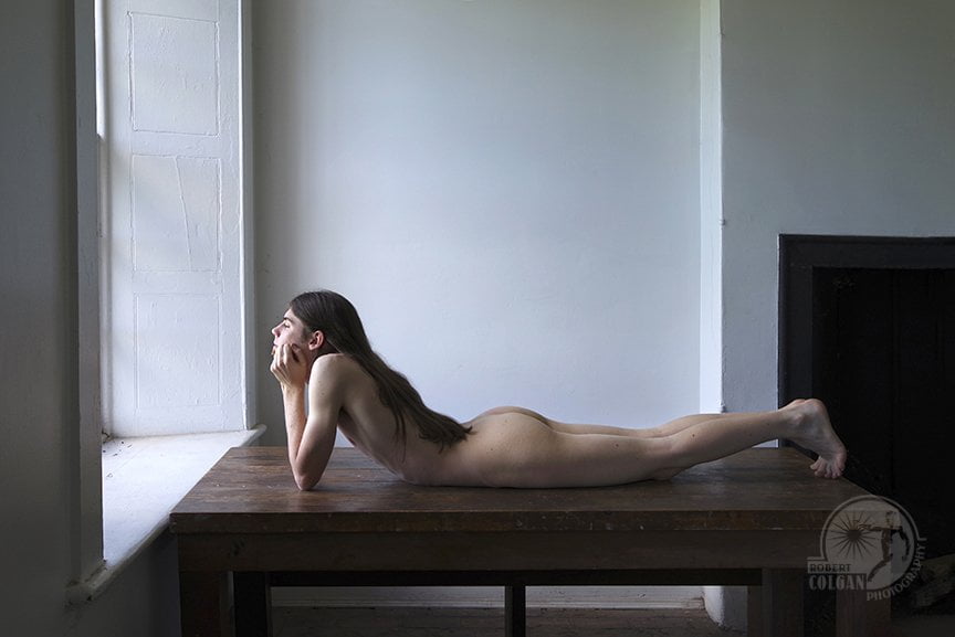 nude man laying on table looking out window