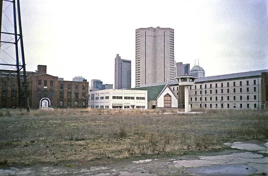 overgrown field with cellblock, chapel and infirmary buildings