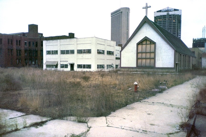 weed covered field with chapel and infirmary buildings