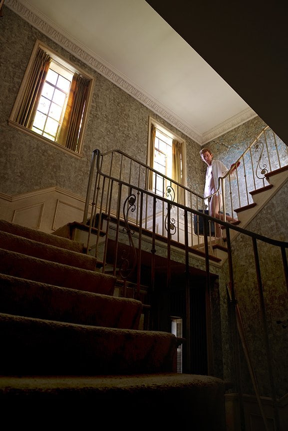 angular shot up stairway, partially nude man holds suitcase