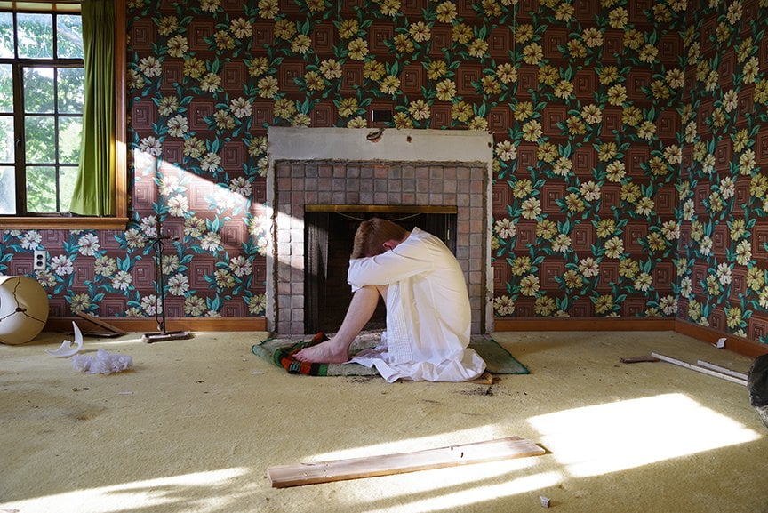 man in tux shirt curled in fetal position in front of fireplace
