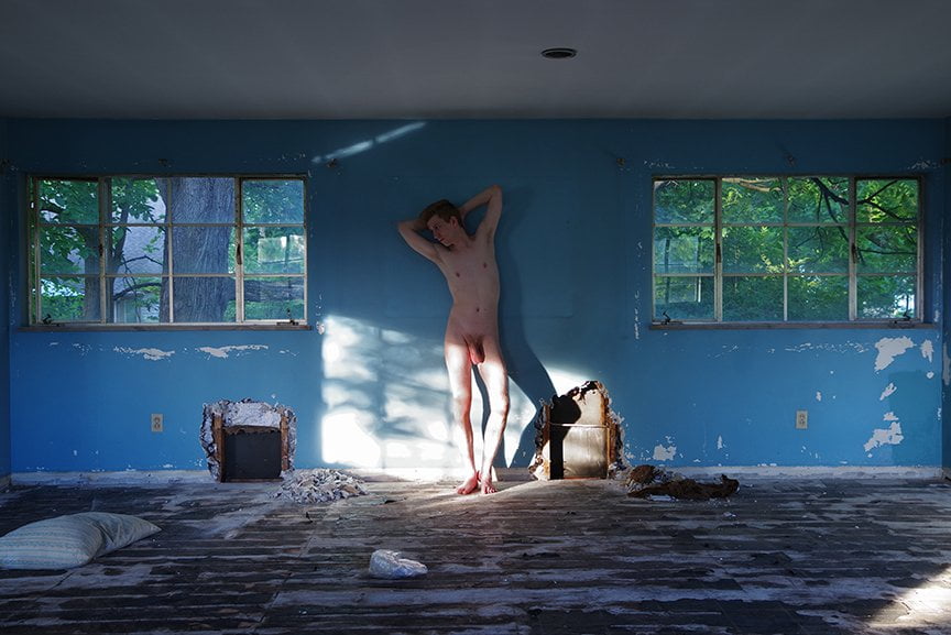 nude man standing between two windows of deserted room