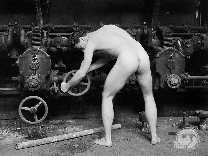 nude man, back turned to camera, turning a wheel on a machine