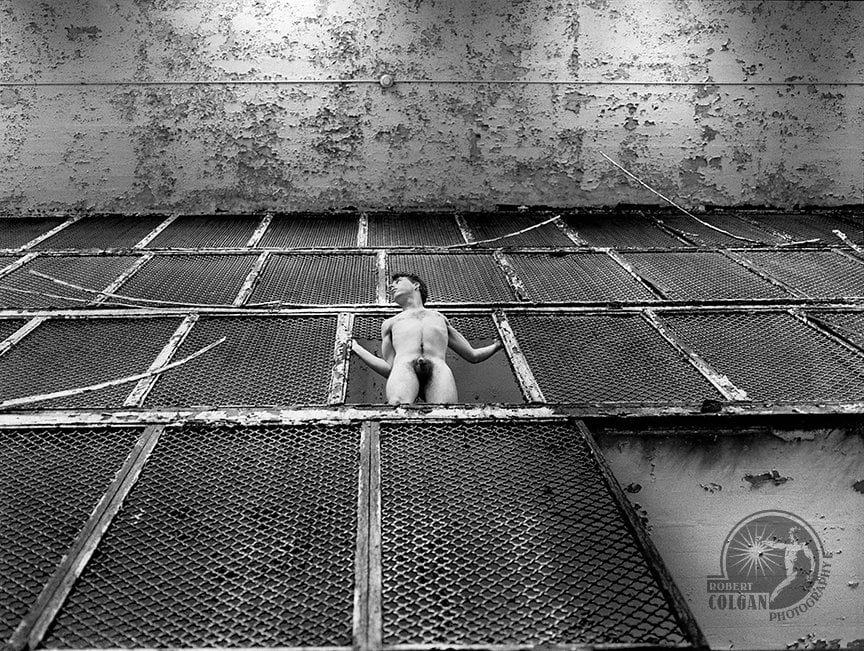 looking up side of cellblock cages with nude man leaning out from missing grate