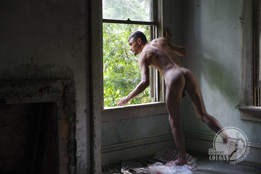 nude man looking out window of abandoned house - it's very dark inside