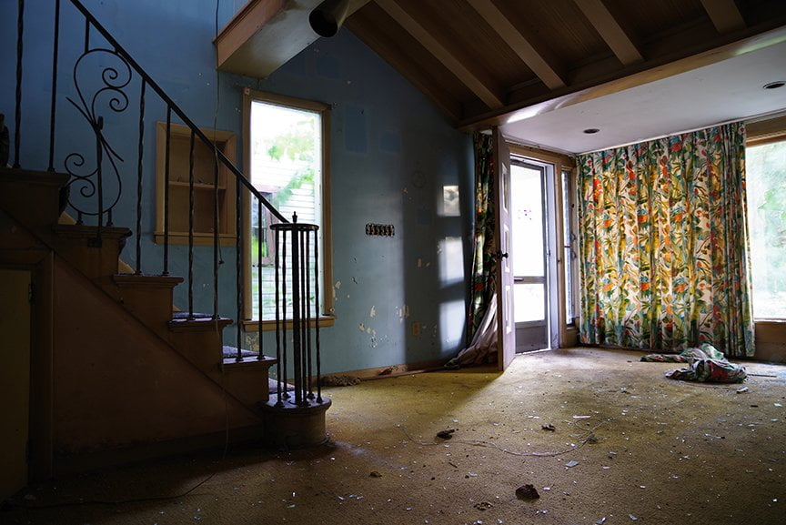 dark interior with bright floral curtains, trash on floor and stairs leading up