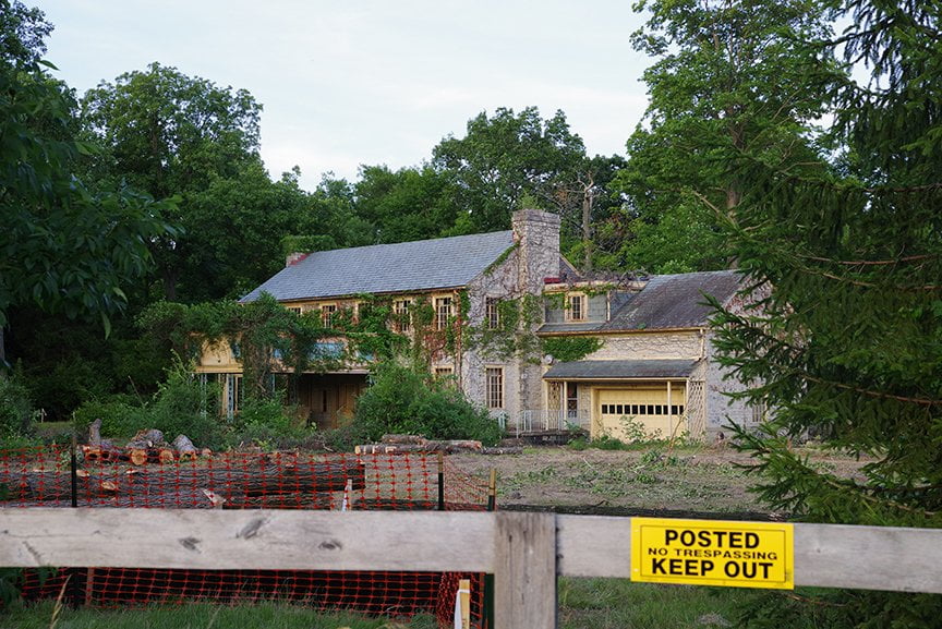 front of house shot from road with no trespassing sign, home covered with vines