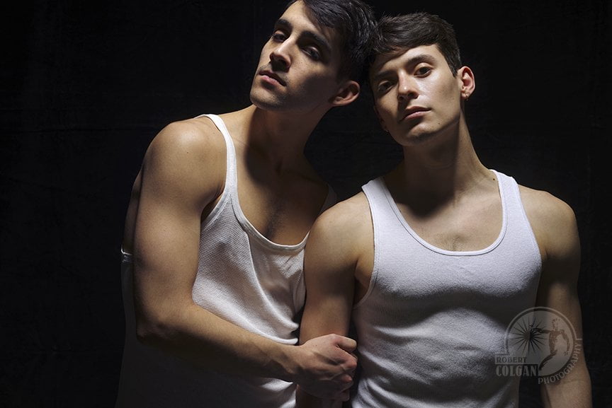 Two men in white muscle shirts stare at the camera
