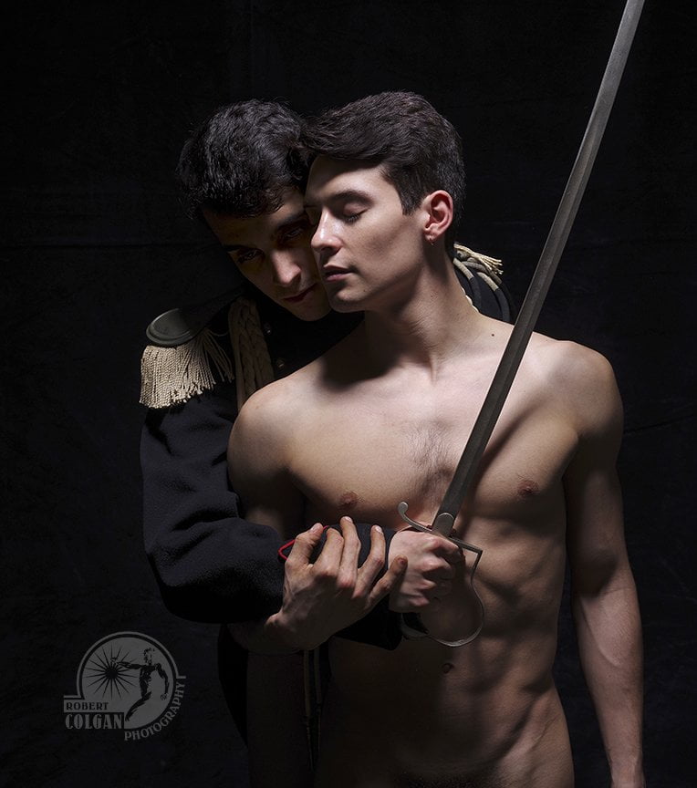 Nude man with eyes closed is embraced by another in uniform