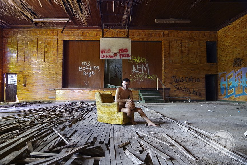 nude man sitting in bright chartreuse chair in abandoned gynmasium