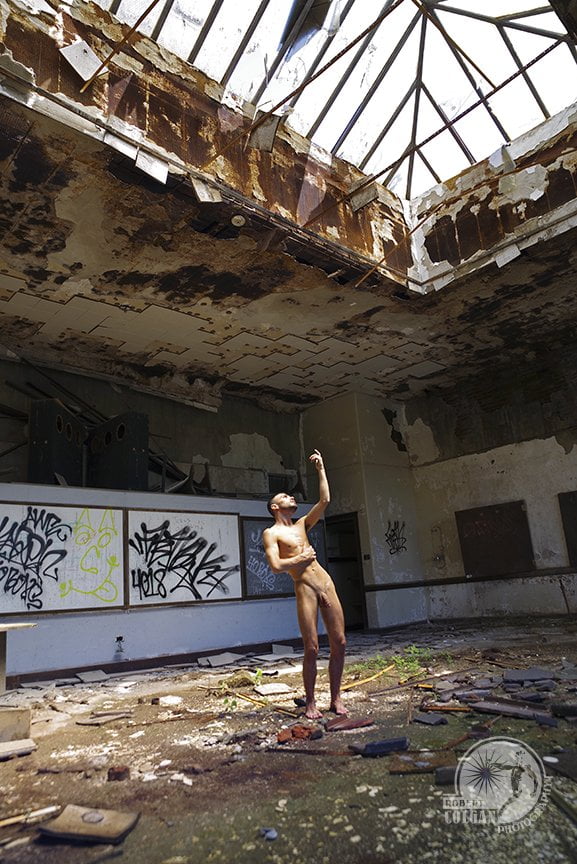 nude man gestures toward broken skylight in old school