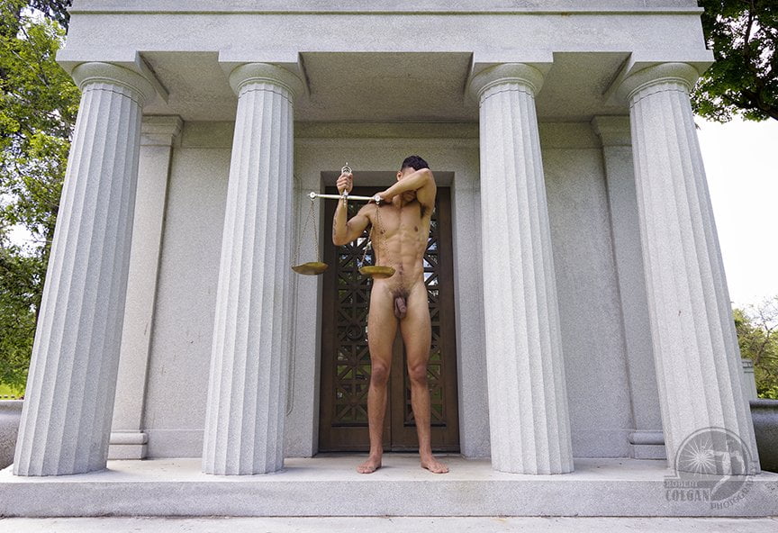 nude man shielding his eyes while holding a set of scales in front of classical structure