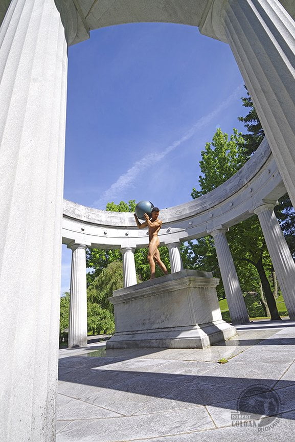 nude man holding huge globe in middle of columned structure outdoors