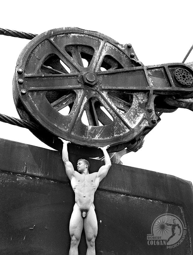 nude man holding giant pulley on bucket