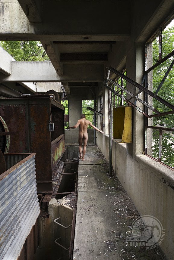 naked man walking away from camera in abandoned industrial building