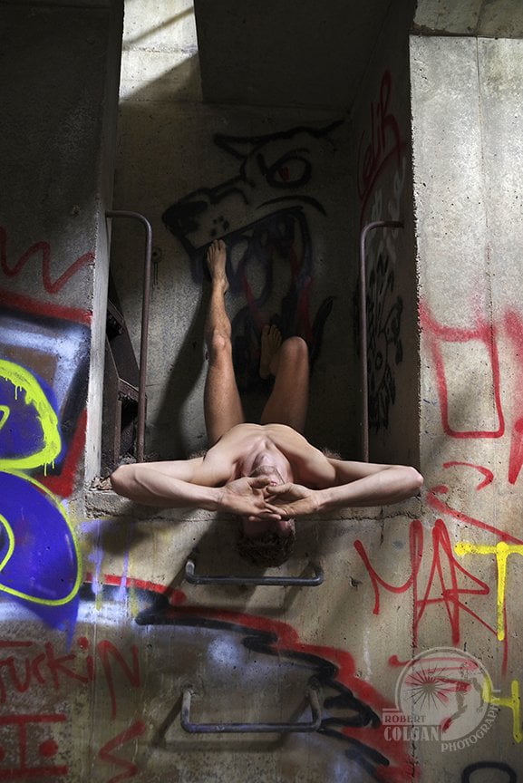 nude man laying in a gangway on his back, hands in front of face