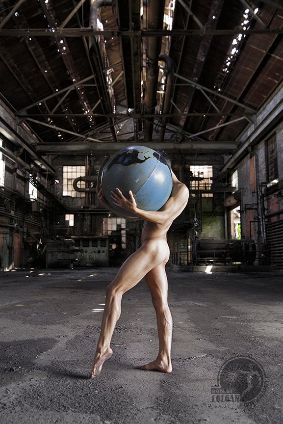 nude male figure carrying huge globe in abandoned industrial setting