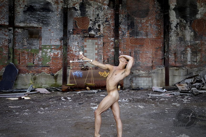 nude man with arm extended, holding scales, in abandoned factory