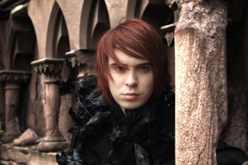 gothically dressed young man with red hair in front of gothic structure