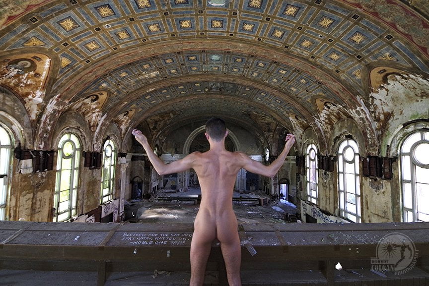 nude man with back to the camera, arms raised, in derelict church