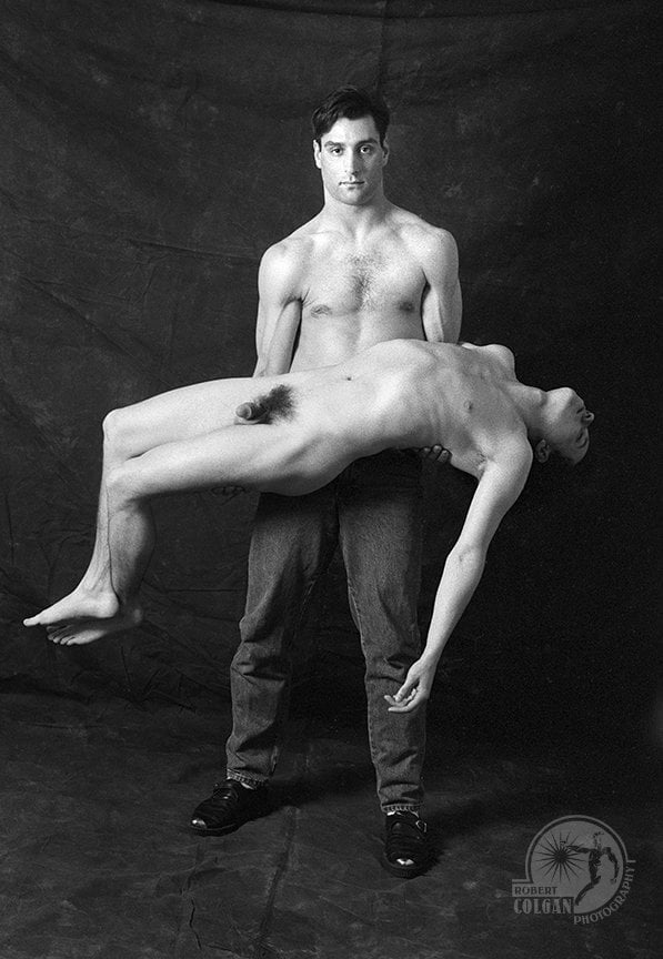 shirtless man holds limp nude body of another man