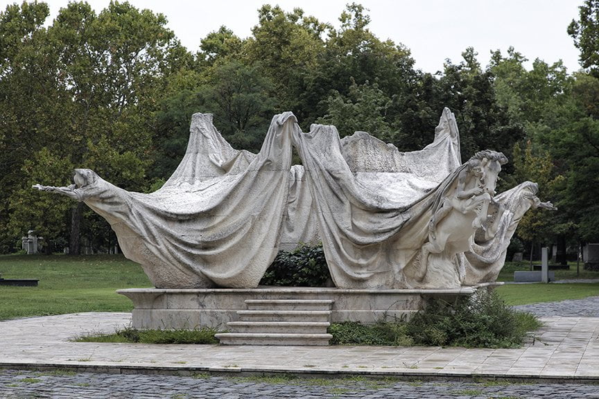 carved tent-like tomb with figures and horses pulling at the corners