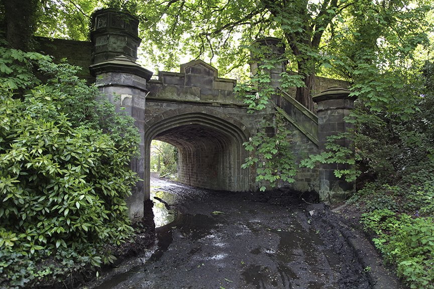 muddy road going under ornate stone bridge in cemetery