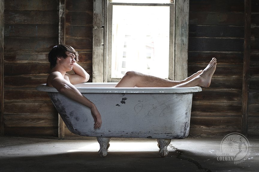 dark haired man lounging in old tub in old building