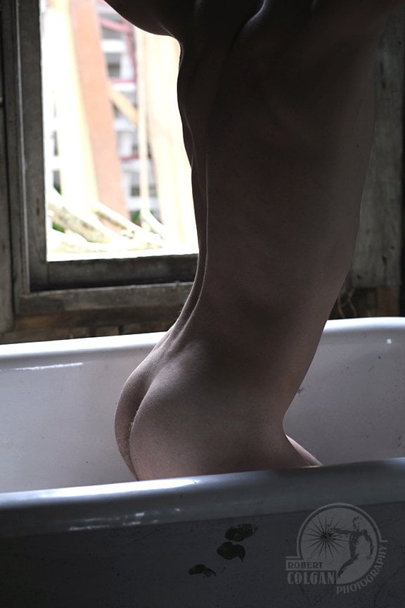 nude torso of man arching back while in tub by open window