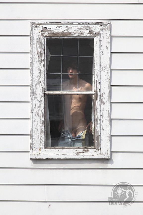 man undresses in front of window, staring at the camera