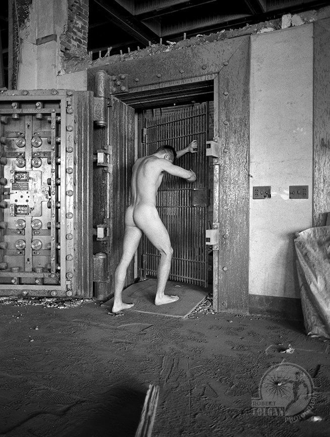 nude man grasps gate of abandoned bank vault door