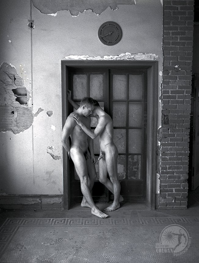 Two nude men stand in front of old elevator