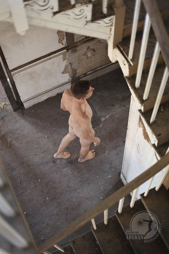 nude man in abandoned house seen from above with stairs wrapping around