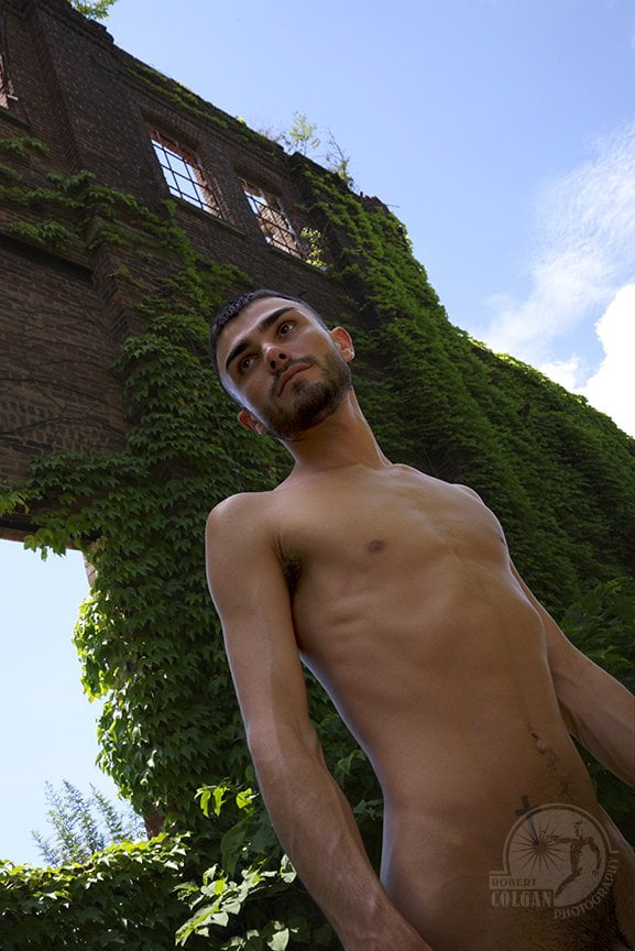 nude man looking up with ivy covered wall of old factory