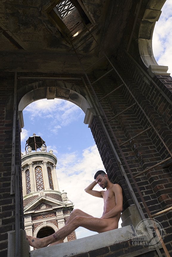 nude man lounging in arched opening of old tower