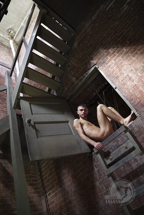 nude man curled in small doorway between stairs