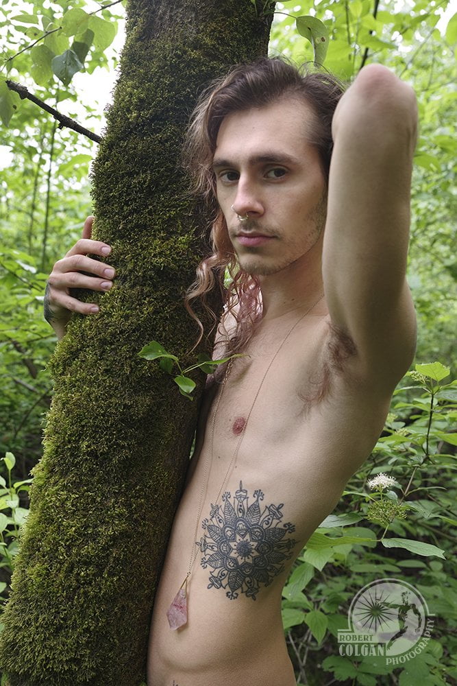 portrait of shirtless man outside grasping mossy tree