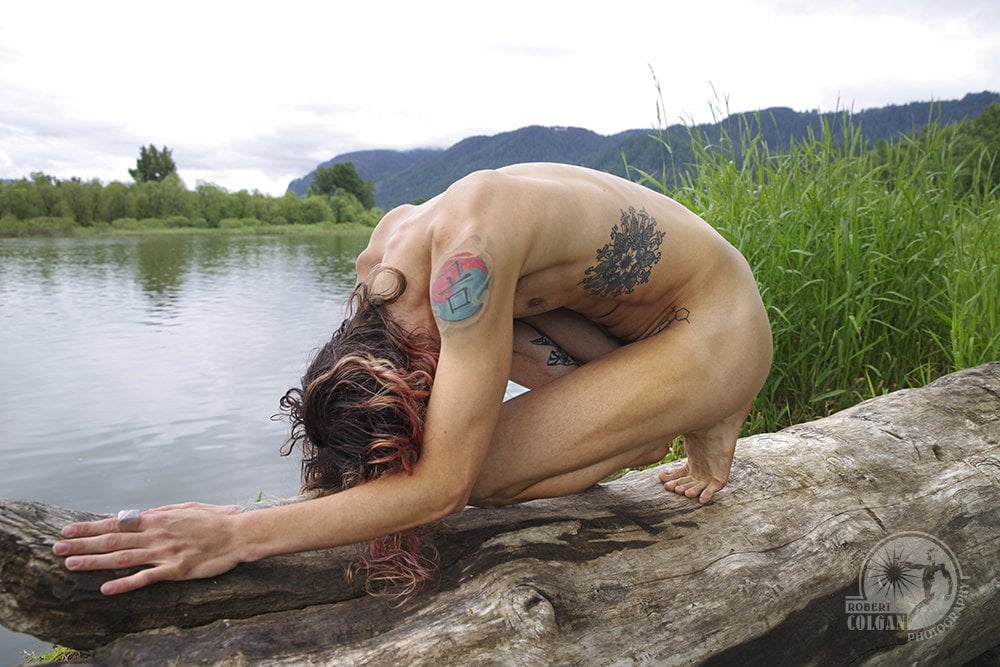 nude man curled up on log by river with hands extended