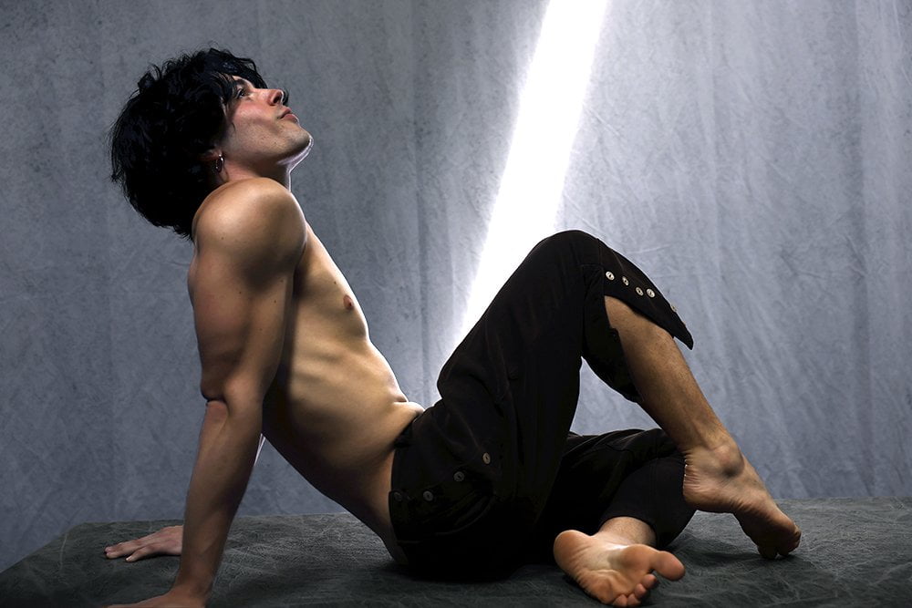 shirtless man sitting back, looking up at sunbeam
