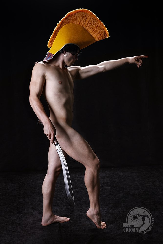 nude man in profile with yellow ceremonial hat holding sword and pointing