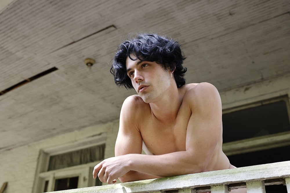 shirtless man looks out from porch
