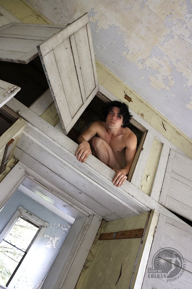 shirtless man stares down at the viewer from overhead cupboards in abandoned house