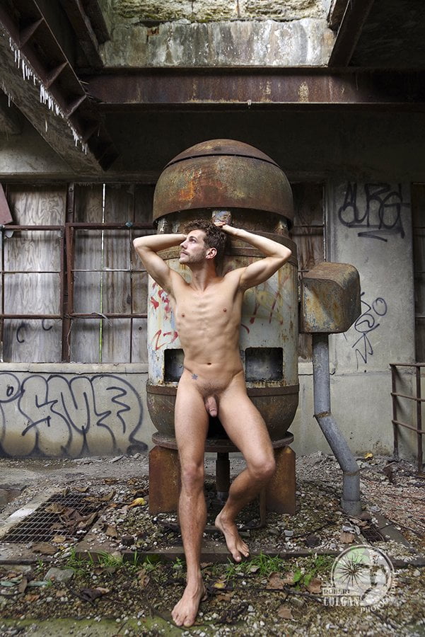nude man leans against old abandoned machinery